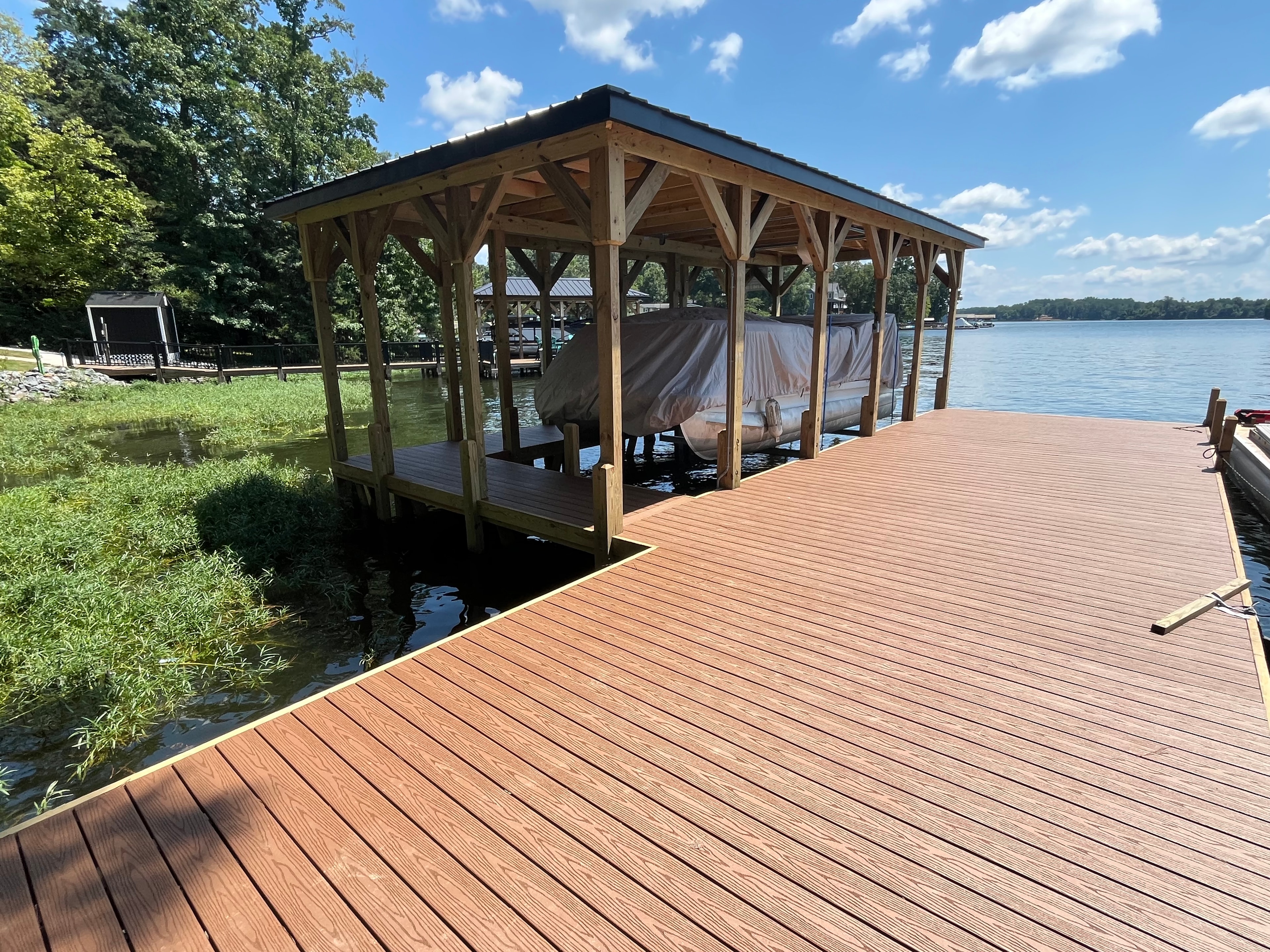 SHT Construction — completed open boathouse with cedar framing, metal roof, and warm composite decking
