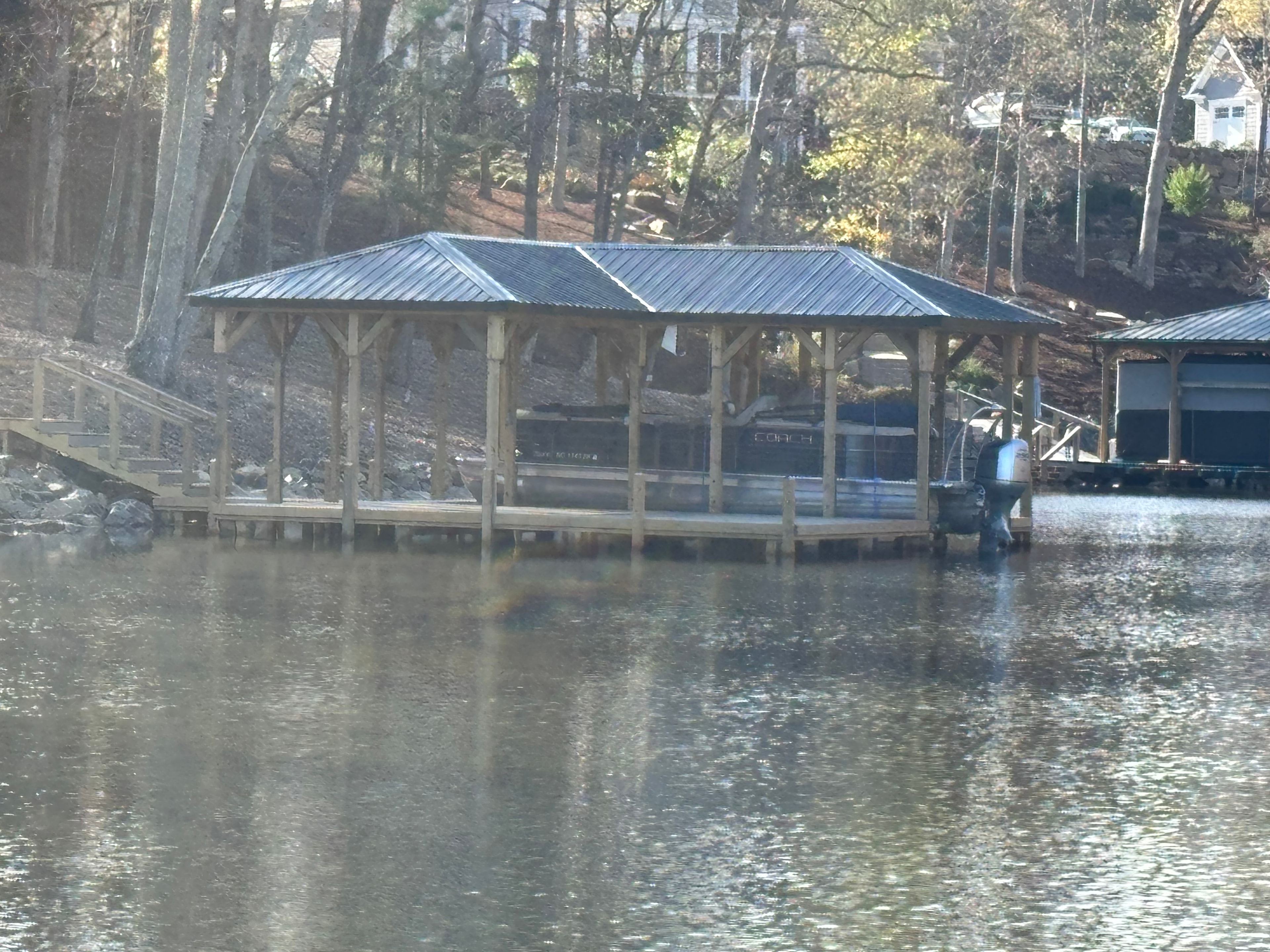 SHT Construction — open timber frame boathouse with metal roof and pontoon boat on the water